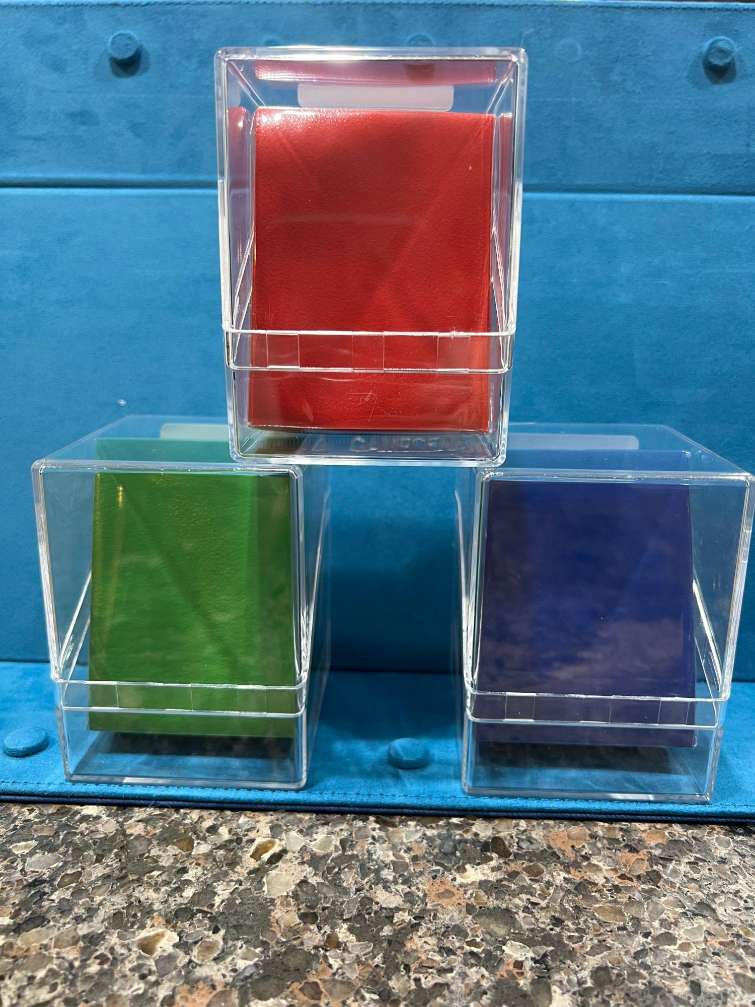 Clear deckboxes holding red, green, and blue sleeved decks